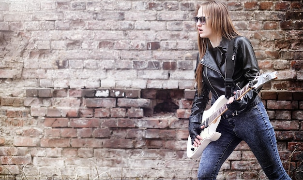 Photo beautiful young girl rocker with electric guitar. a rock musician girl in a leather jacket with a guitar sings. a rock band soloist plays the guitar and screams into the microphone.