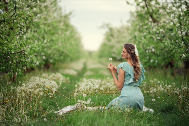 Beautiful young girl in a romantic dress blows on a dandelion