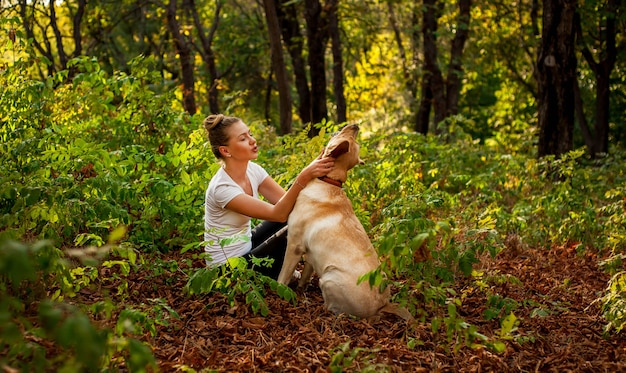 beautiful young girl sitting in the forest with a dog and petting her beloved pet