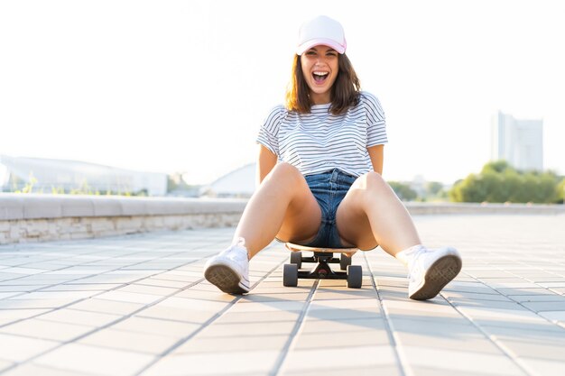 Beautiful young girl sitting on longboard in sunny weather.