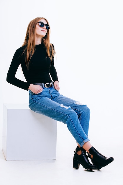 Beautiful young girl sitting on a white cube in the Studio with insulation.