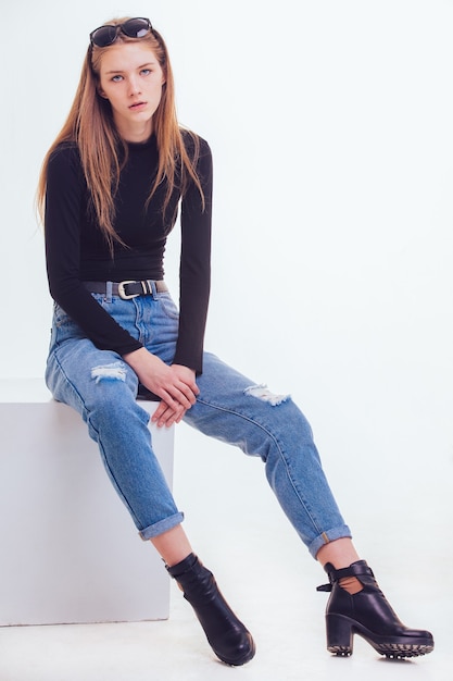 Beautiful young girl sitting on a white cube in the Studio with insulation.