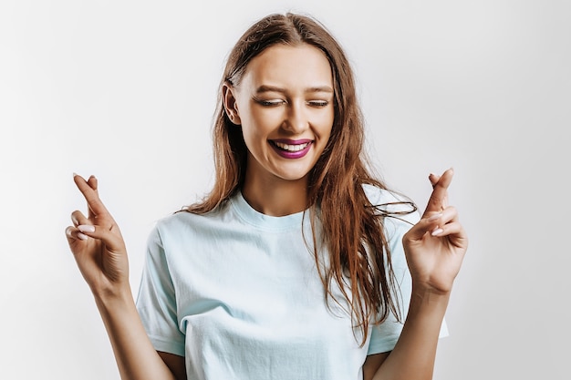 Beautiful young girl smiles crossed her fingers for luck and made a wish on a white isolated gray background