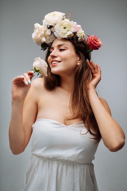 Beautiful young girl smiling and posing with flowers on gray wall in white dress  portrait