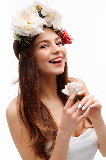 Beautiful young girl smiling and posing with flowers on white wall in white dress  portrait