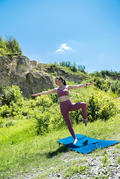 Beautiful young girl in a sports uniform near the rocks is engaged in stretching outdoors