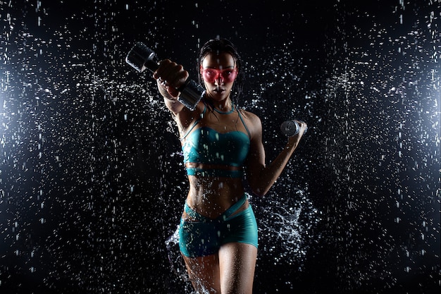 Beautiful young girl in sportswear poses with dumbbells in aqua studio