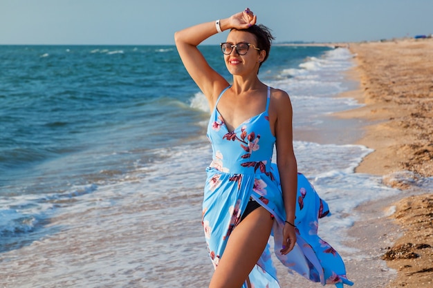 Beautiful young girl standing on the beach by the sea in a blue dress. The girl on the beach in a dress near the sea.