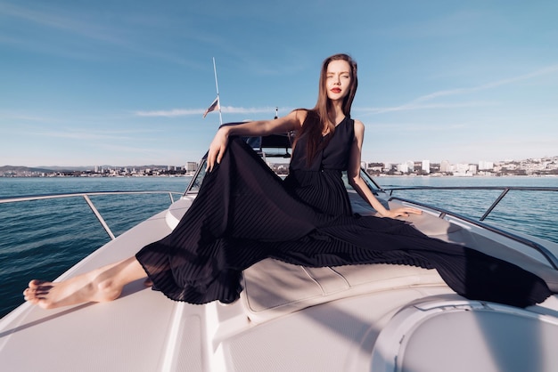 Beautiful young girl in stylish black summer clothes resting on her white yacht, enjoying a vacation at sea