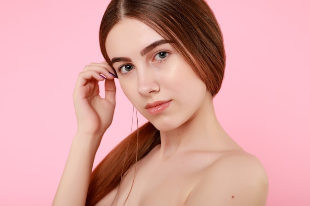 Beautiful young girl touching her perfect skin on pink background. Skin care concept. Beauty Woman Portrait with clean skin. Beauty cute fashion model with natural make up on pink background