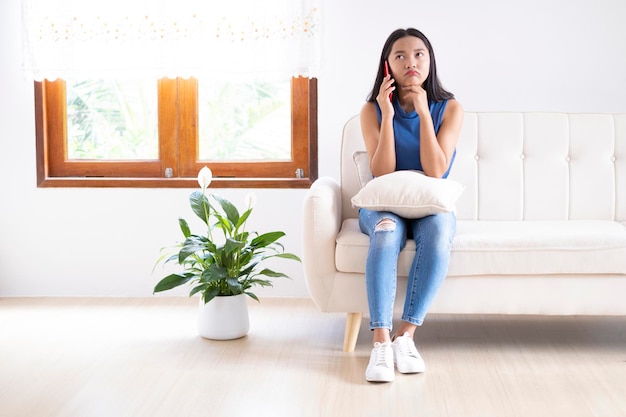 Beautiful young girl use smartphone sitting on sofa at home