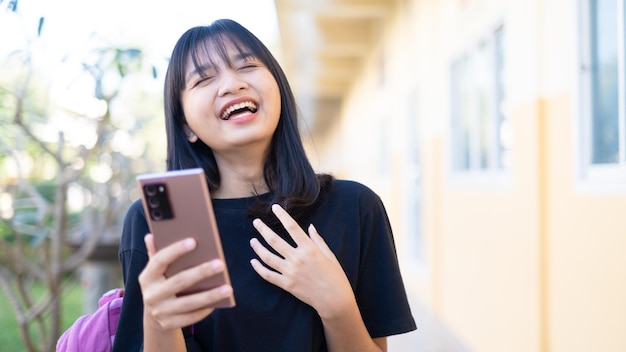 Beautiful young girl useing smart phone at school,Asian girl,Orange background.