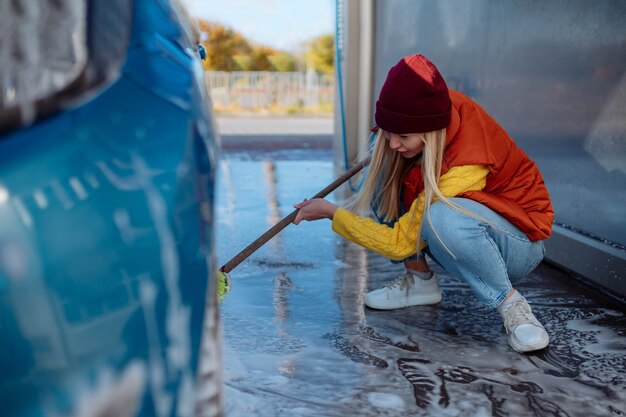 Beautiful young girl washes the car at the self-service car wash. erasing dirt to the car with a brush