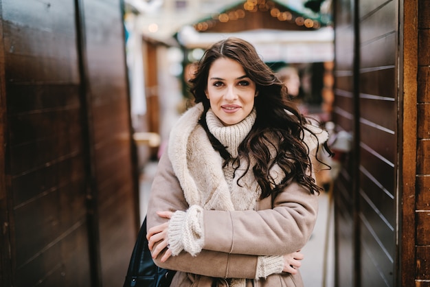 Beautiful young girl in winter coat standing in street and enjoying at nice winter day. Looking at camera and smiling.