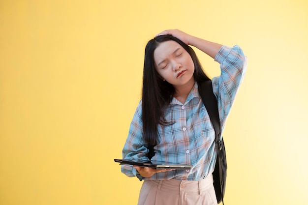 Beautiful young girl with backpack and hold laptop on yellow background.