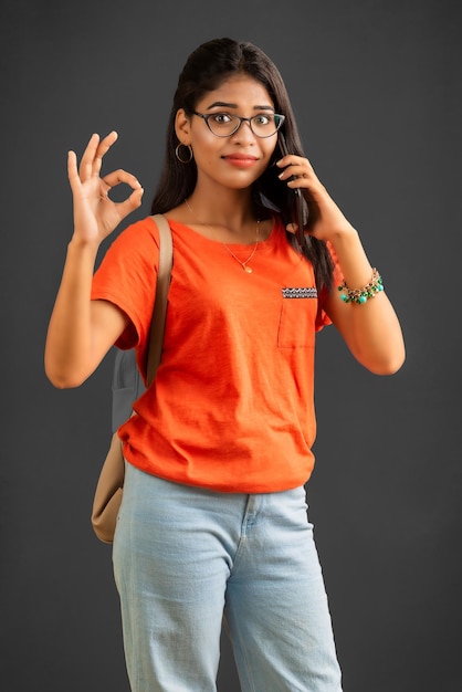 Beautiful young girl with a backpack using mobile phone or smartphone on gray background