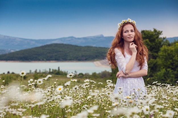 Beautiful young girl with curly red hair in camomile field