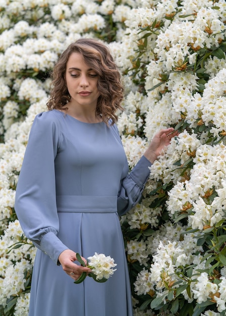 A beautiful young girl with dark wavy hair among white rhododendron flowers