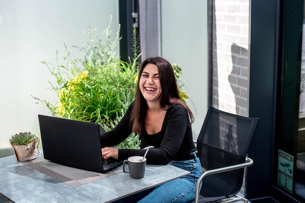 beautiful young girl with a laptop sits at a table and works