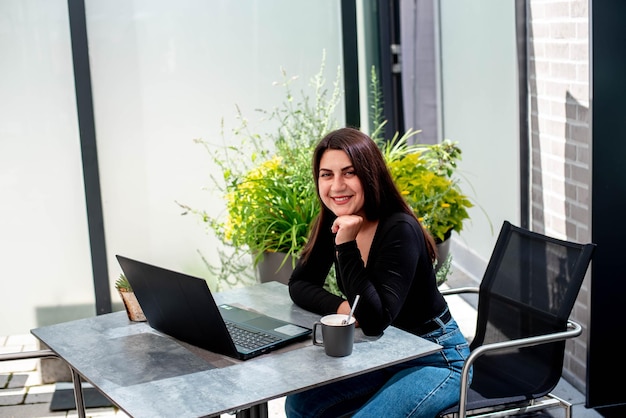 Beautiful young girl with a laptop, sitting at the table smiling and working on a laptop