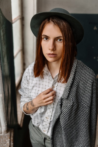 Beautiful young  girl with long hair, wears a stylish hat, a gray coat, a white shirt and pants