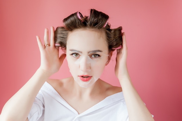 Beautiful young girl with a mask and curlers touching her face.