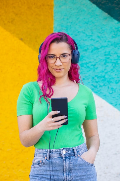 Beautiful young girl with pink hair and glasses listening to music on headphones street style colo