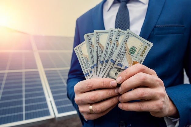 Beautiful young hand in a blue jacket holds dollars near the new solar panels