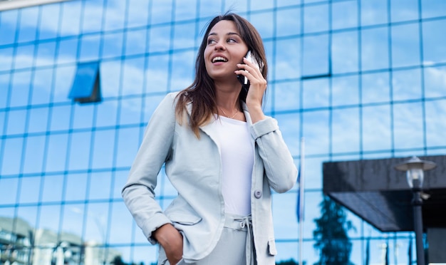 A beautiful young happy business lady standing in city street and speaking on mobile phone conversation