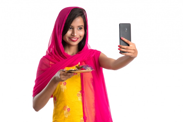 Beautiful young happy girl taking selfie with pooja thali using a mobile phone or smartphone