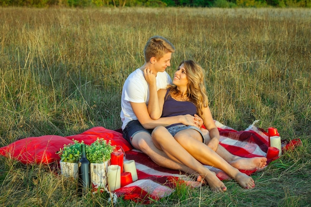 Beautiful young happy loving couple on picnic lying down on plaid on sunny summer day enjoying and resting. hugging and looking at each other and smiling.