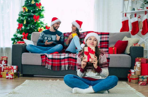 beautiful young happy smiling woman in a Christmas sweater and Santa hat is holding a gift box