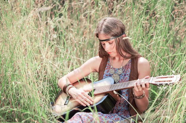 Beautiful young hippie woman playing guitar sitting on grass