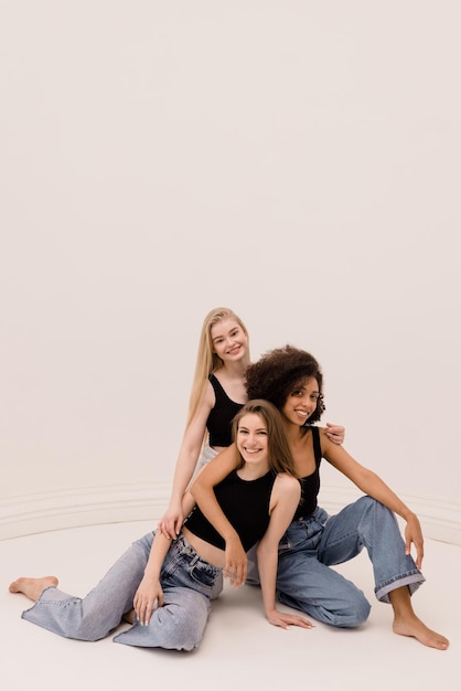 Beautiful young interracial girls wear black tops and jeans stand barefoot in pile on white background