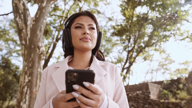 Beautiful young Latin woman using smartphone standing on city street Portrait of Latina smiling female using mobile phone