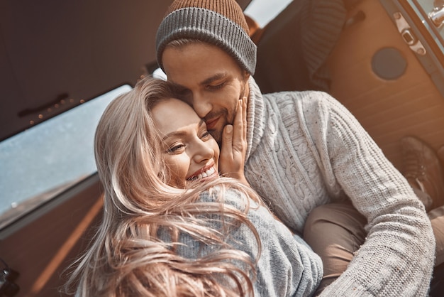 Beautiful young loving couple embracing and smiling while spending time in their minivan