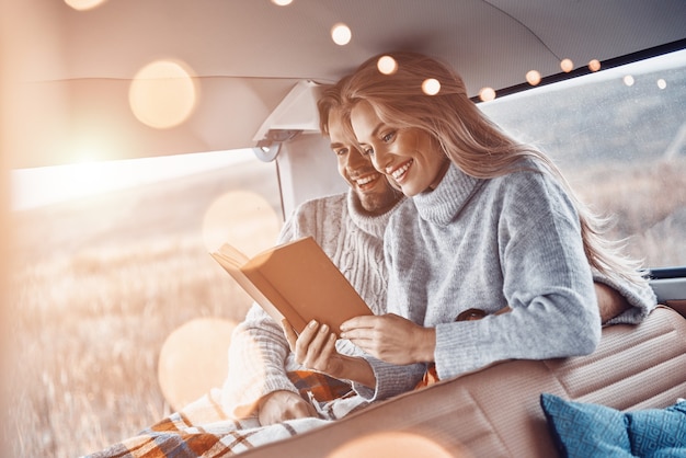 Beautiful young loving couple reading book together and smiling while spending time in their minivan