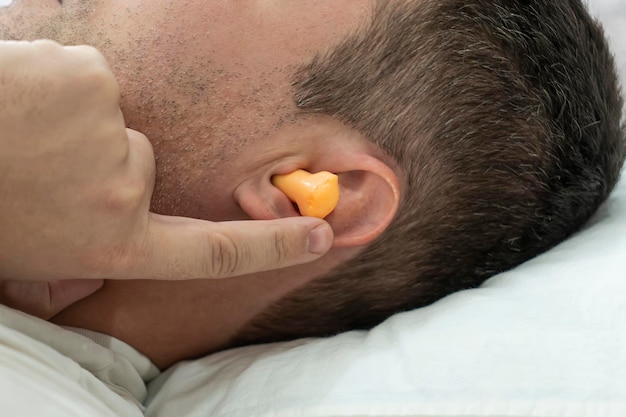 Beautiful young man sleeping in the ears orange earplugs against street noise salvation from noisy neighbors when prevent sleep plug in the ears for silence during sleep