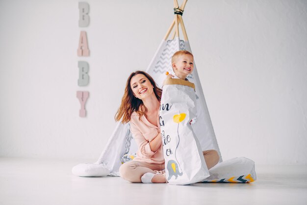 A beautiful young mom and her little son having fun in the light room. Little smiling boy with candy get out of a paper eco-bag.