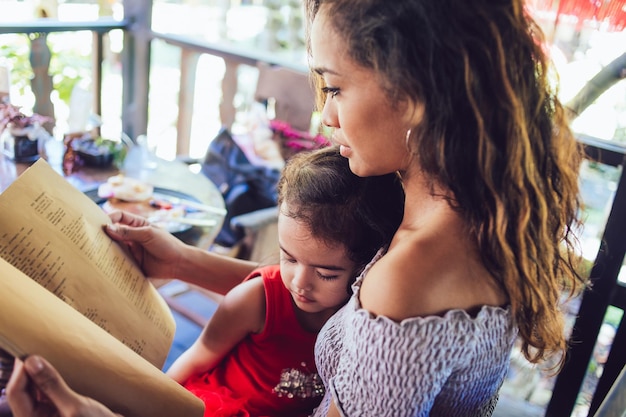 Beautiful young mother and cute little daughter cheeking menu at cafe