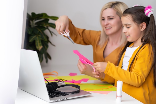 Photo beautiful young mother helping her younger daughter with homework.