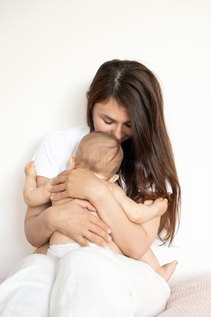 A beautiful young mother plays and cuddles with her baby in her bedroom on the bed Love motherhood Weasel tenderness Lifestyle