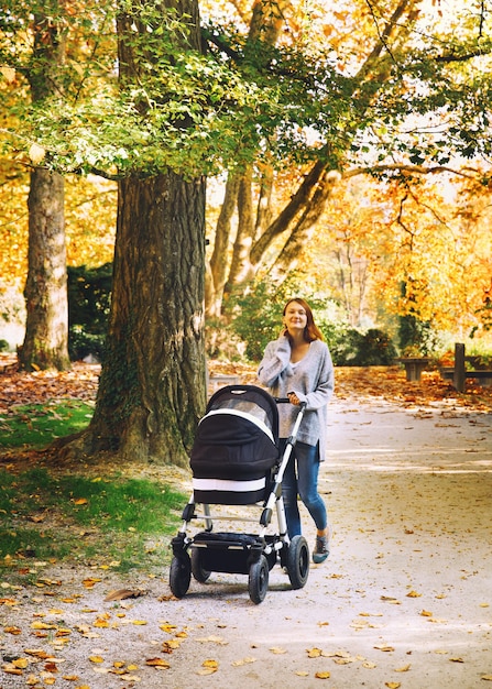 Beautiful young mother with baby carriage walking in autumn park