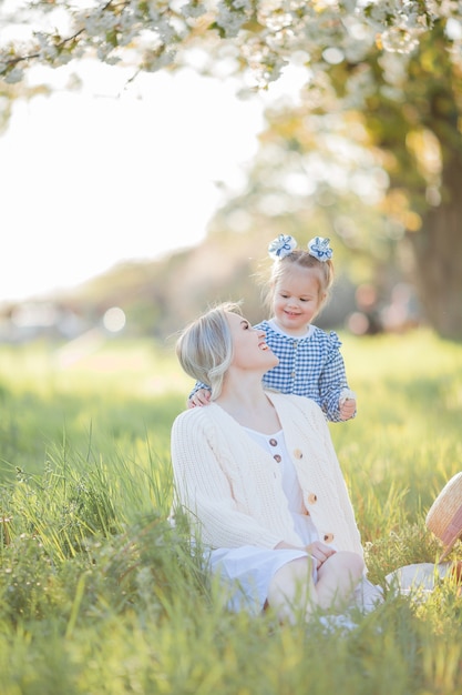 A beautiful young mother with her little daughter are resting on a picnic in the flowering garden