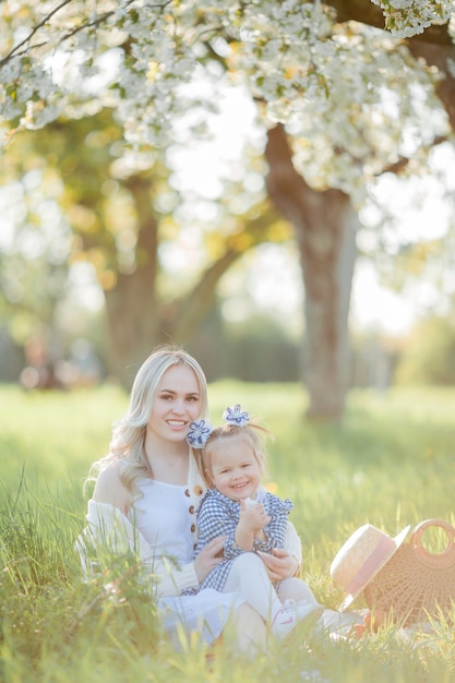 Photo a beautiful young mother with her little daughter are resting on a picnic in the flowering garden