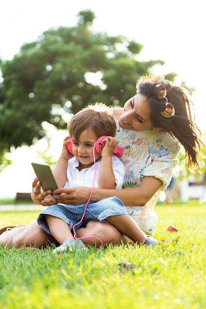 Beautiful young mother with her son listening to music in the park.