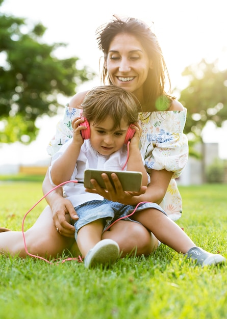 Beautiful young mother with her son listening to music in the park.