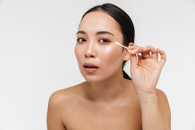 beautiful young pretty asian woman with healthy skin posing naked isolated over white wall holding cotton buds.