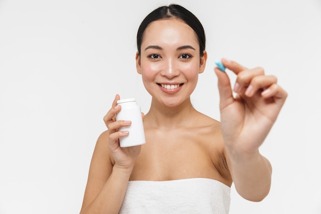 beautiful young pretty asian woman with healthy skin posing naked isolated over white wall holding vitamins pill.