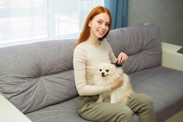 beautiful young red-haired female combing her dog